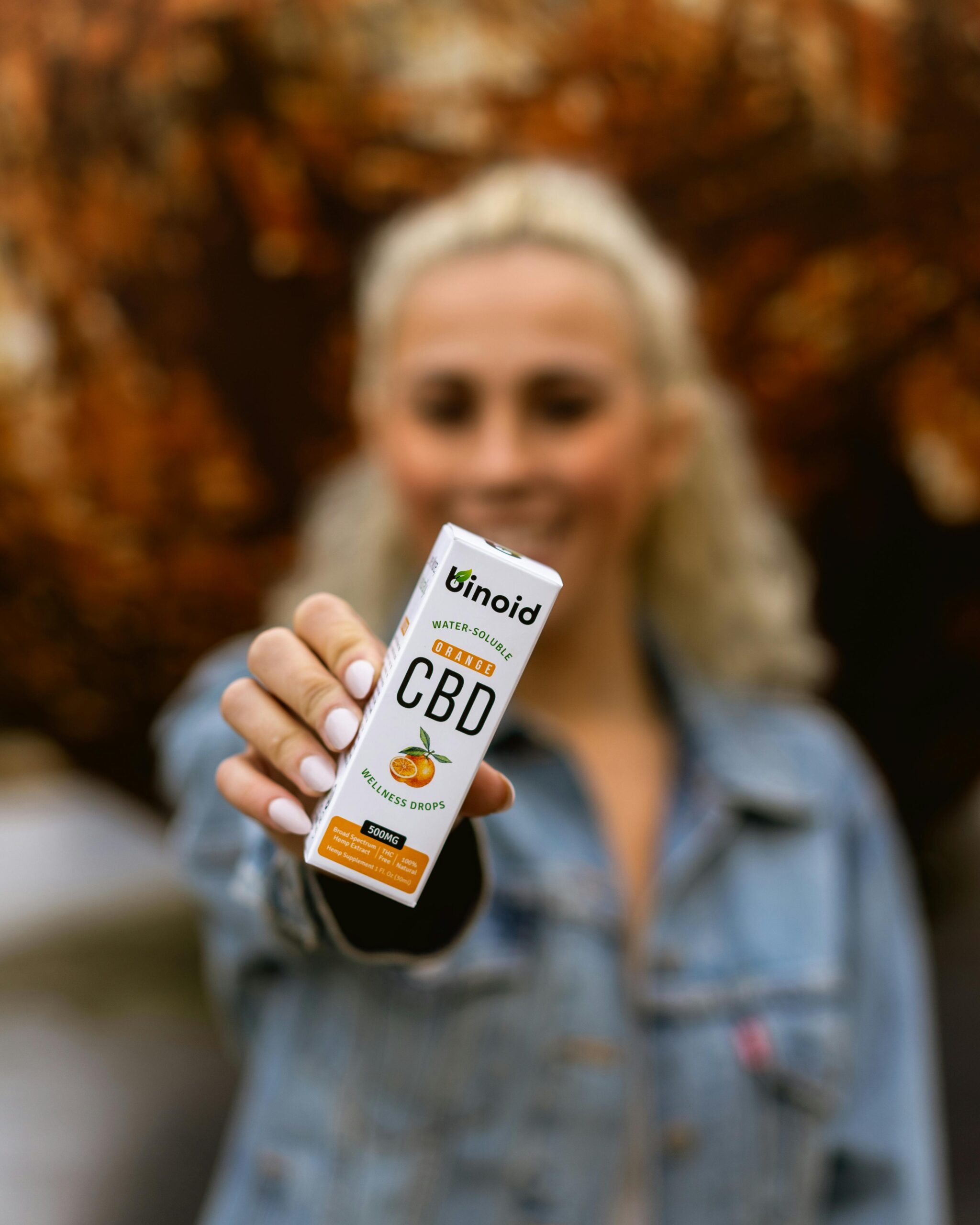 Focus on a woman presenting Binoid CBD oil with an autumn background. Promotes wellness and health.